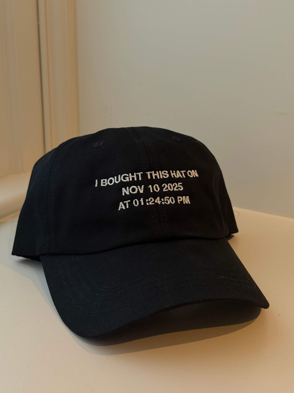 Black cap with embroidered timestamp on a white surface