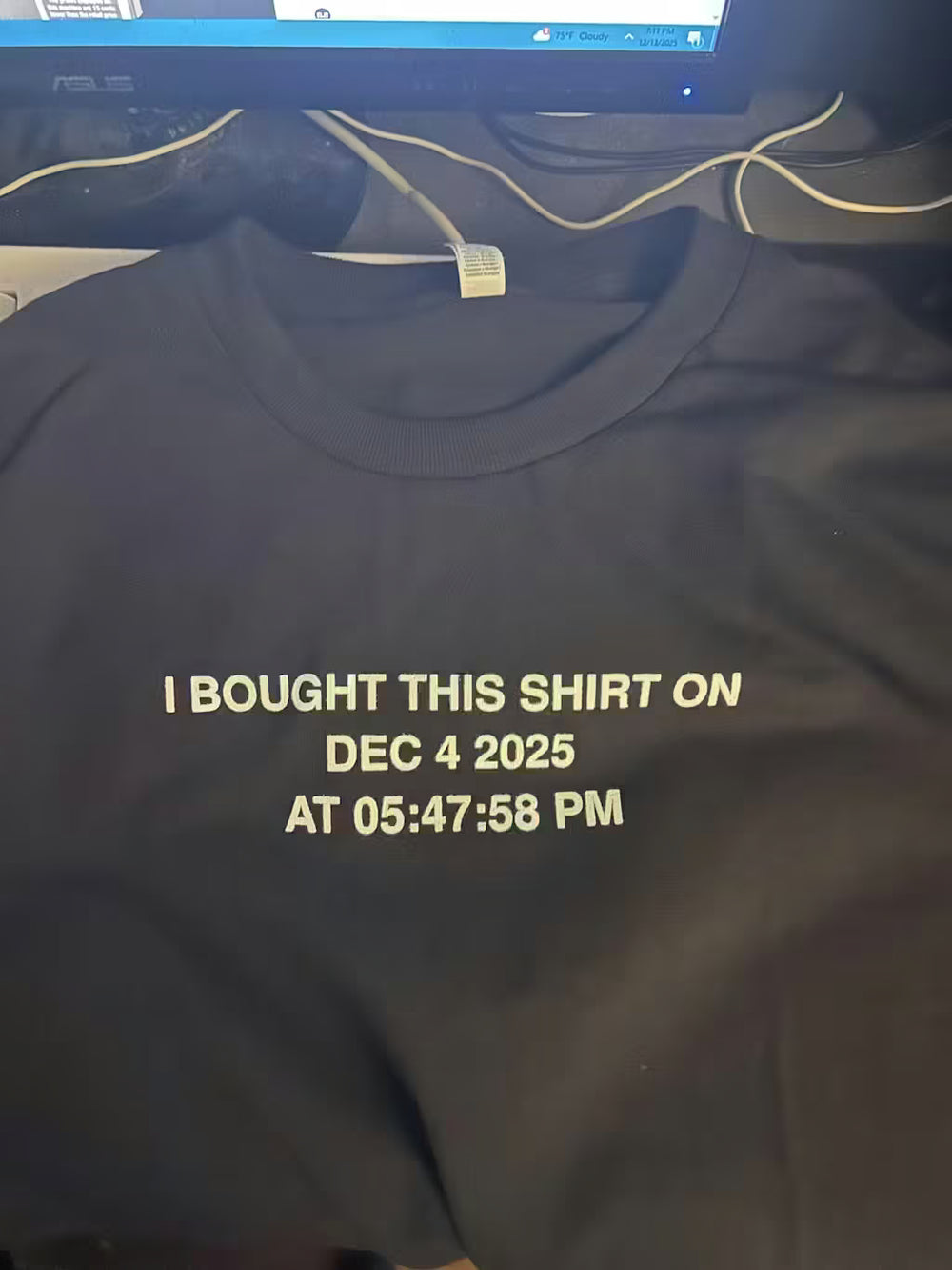 Black shirt with text 'I bought this shirt on Dec 4 2025 at 05:47:58 PM' on a dark background