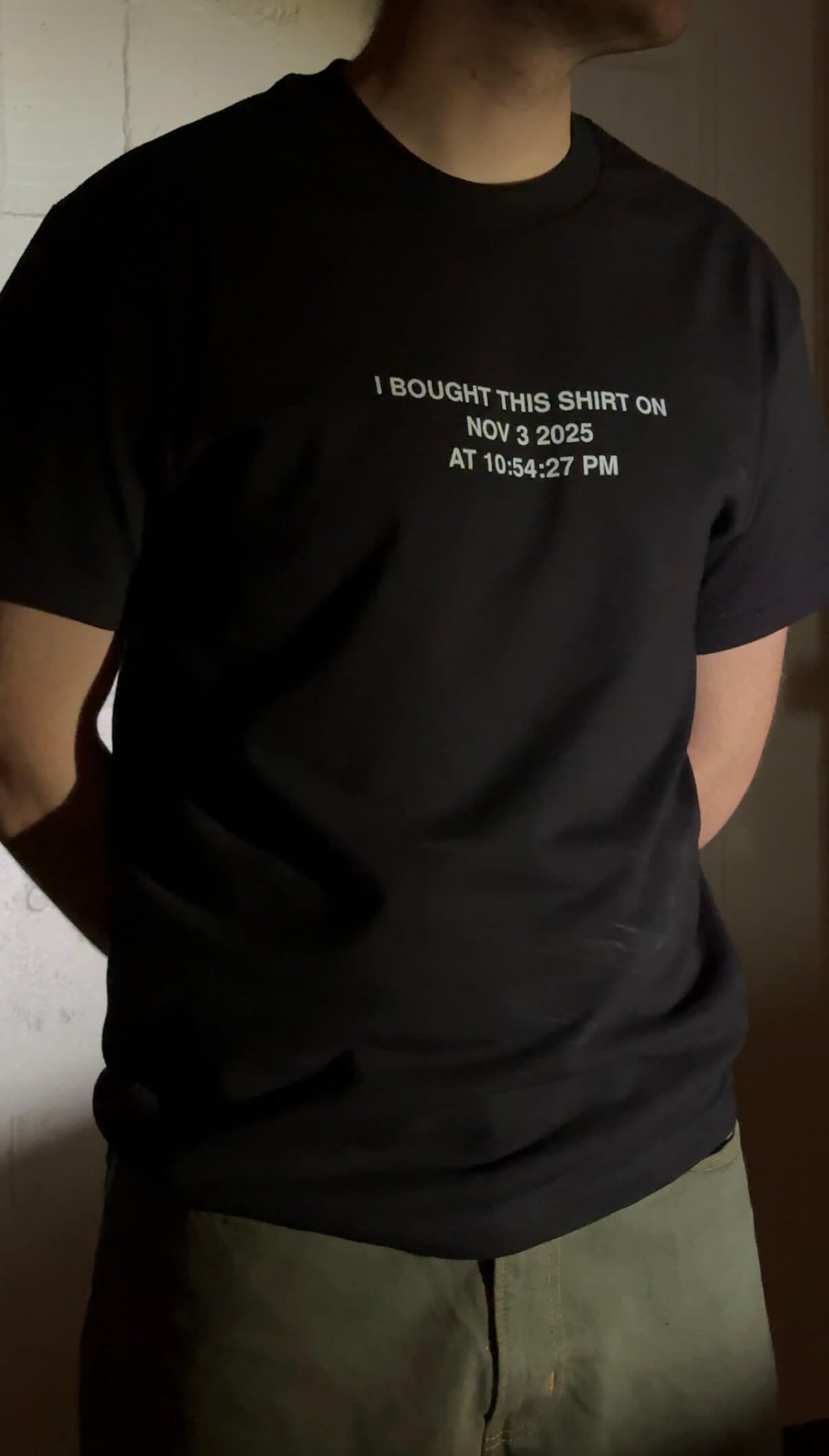Person wearing a black t-shirt with timestamp on it, standing against a plain background.